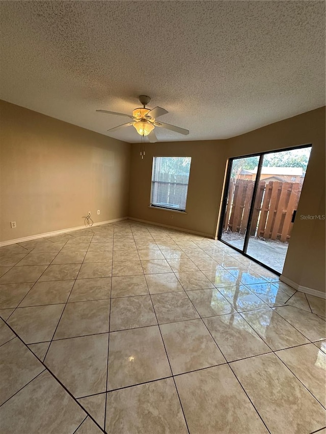 empty room with healthy amount of natural light, ceiling fan, baseboards, a textured ceiling, and light tile patterned floors