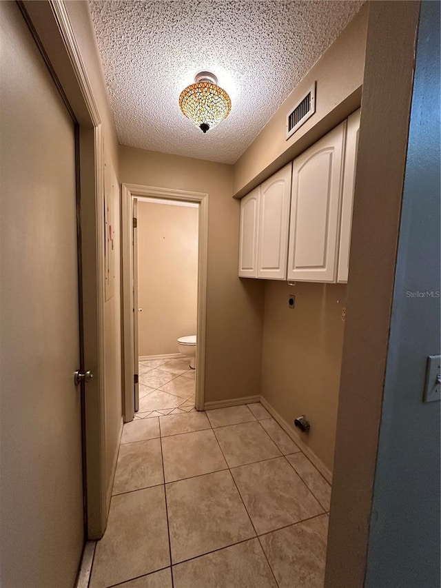 washroom featuring cabinet space, a textured ceiling, light tile patterned floors, hookup for an electric dryer, and baseboards
