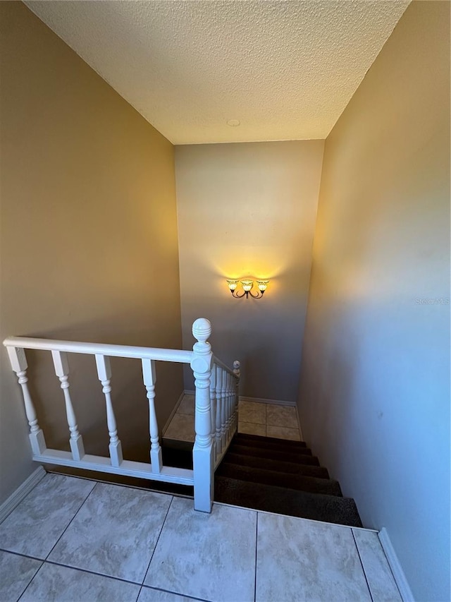 stairs featuring baseboards, tile patterned flooring, and a textured ceiling