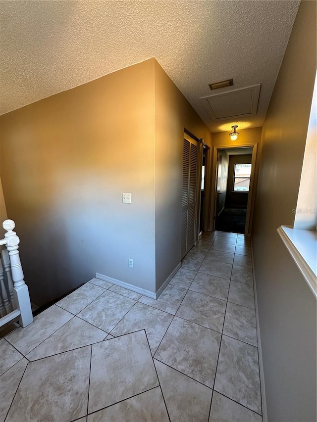 corridor with a textured ceiling, light tile patterned floors, and baseboards
