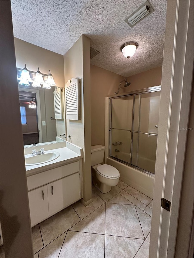 bathroom featuring a textured ceiling, toilet, combined bath / shower with glass door, vanity, and tile patterned flooring