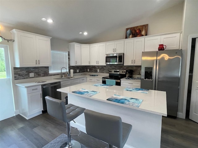 kitchen featuring appliances with stainless steel finishes, a sink, dark wood-type flooring, tasteful backsplash, and vaulted ceiling