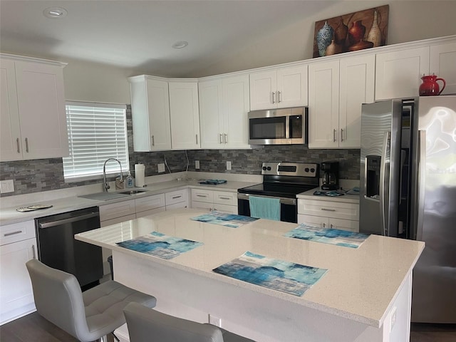 kitchen featuring stainless steel appliances, a sink, a breakfast bar, white cabinets, and tasteful backsplash
