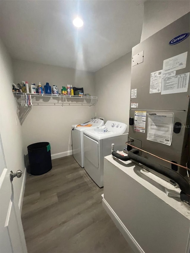 washroom with washing machine and dryer, heating unit, wood finished floors, and baseboards