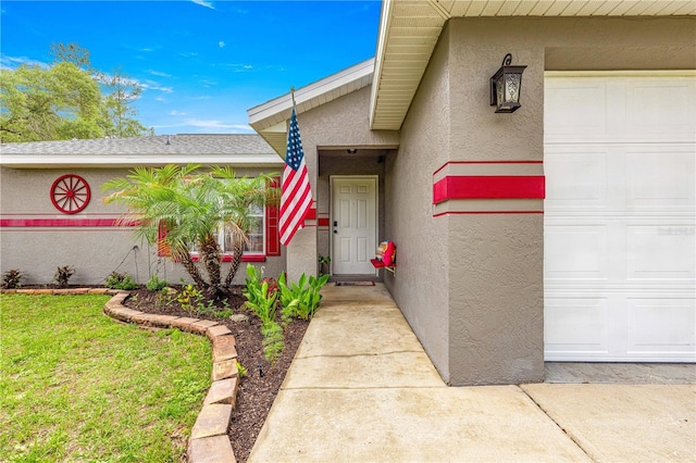 view of exterior entry with stucco siding, a garage, and a lawn