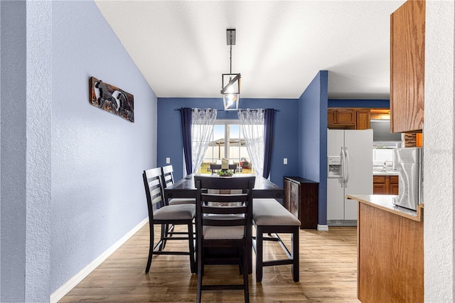 dining room featuring a textured wall, light wood-type flooring, and baseboards