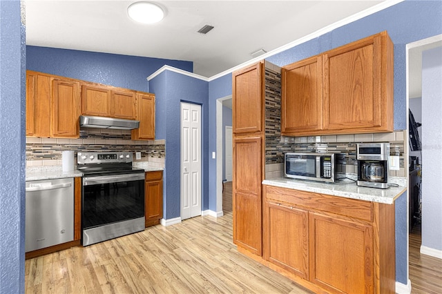 kitchen with appliances with stainless steel finishes, under cabinet range hood, tasteful backsplash, light wood finished floors, and a textured wall