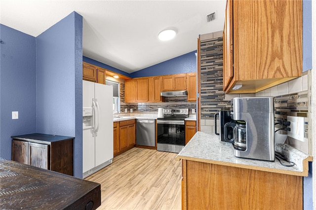 kitchen featuring appliances with stainless steel finishes, decorative backsplash, light wood-style flooring, vaulted ceiling, and brown cabinets