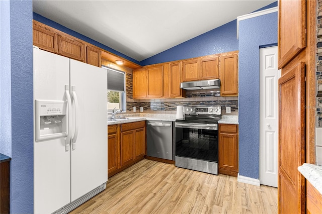 kitchen with stainless steel appliances, vaulted ceiling, light wood finished floors, light countertops, and a textured wall