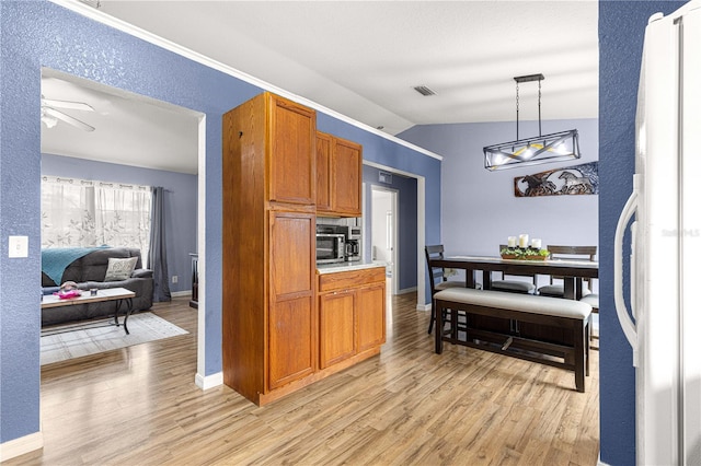 kitchen featuring freestanding refrigerator, light wood-type flooring, brown cabinetry, and lofted ceiling