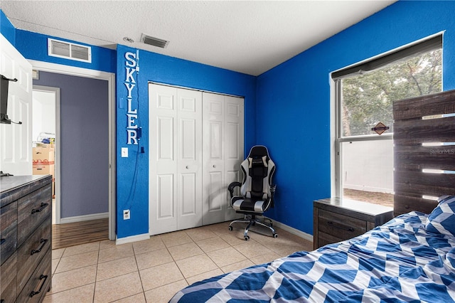 bedroom with baseboards, light tile patterned flooring, a closet, and a textured ceiling