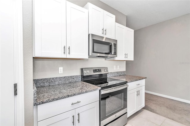 kitchen featuring stainless steel appliances, dark stone counters, white cabinets, and light colored carpet