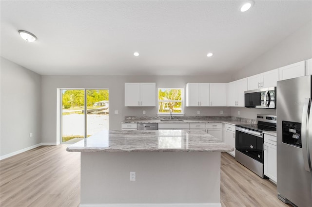 25 Juniper Pass Way, Ocala, FL 34480 - kitchen with stainless steel appliances, a center island, light stone countertops, light wood-style floors, and white cabinetry