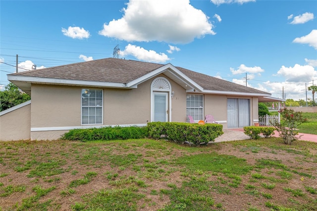 ranch-style home with stucco siding, a shingled roof, and a front lawn