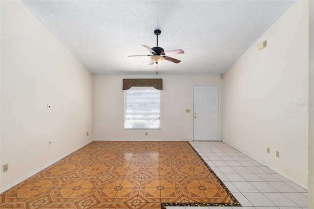 empty room with a ceiling fan, a textured ceiling, light tile patterned floors, and baseboards