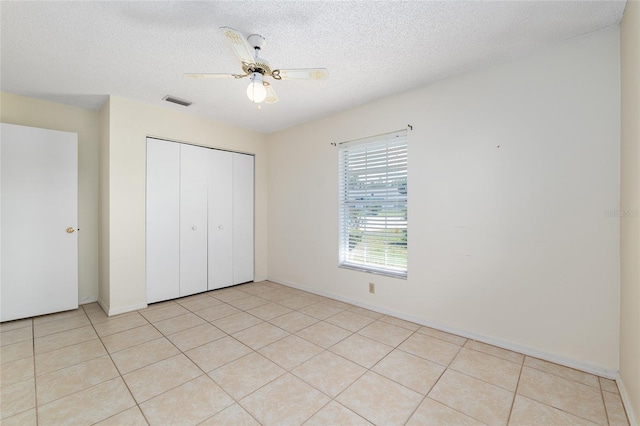 unfurnished bedroom with a closet, light tile patterned flooring, a textured ceiling, a ceiling fan, and baseboards