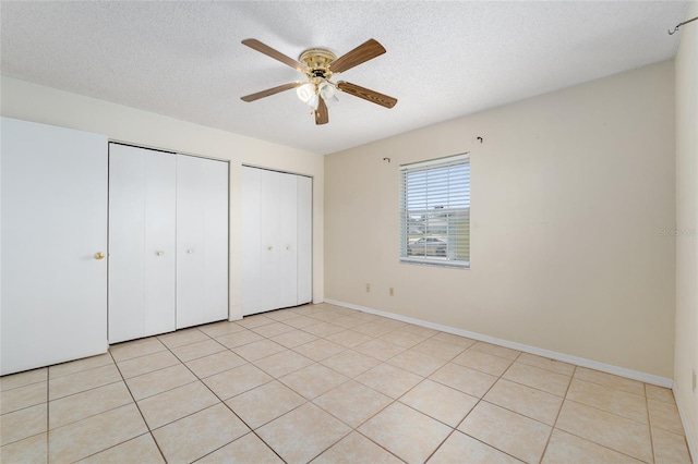 unfurnished bedroom with two closets, a textured ceiling, light tile patterned flooring, ceiling fan, and baseboards