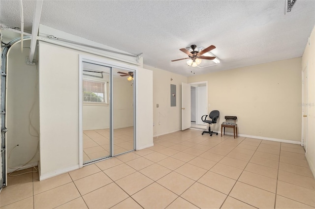 interior space featuring electric panel, a textured ceiling, light tile patterned floors, a ceiling fan, and baseboards