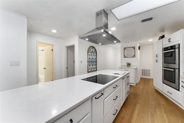 2146 NE 9th St, Ocala, FL 34470 - kitchen with island exhaust hood, stainless steel double oven, black electric stovetop, recessed lighting, and white cabinets