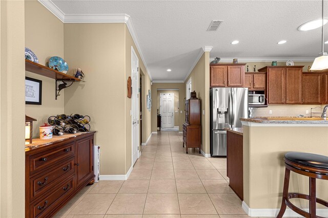 9642 SW 95th Loop, Ocala, FL 34481 - kitchen featuring stainless steel appliances, brown cabinetry, crown molding, a kitchen breakfast bar, and light tile patterned flooring