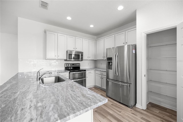 7270 SW 99th Cir, Ocala, FL 34481 - kitchen with stainless steel appliances, a sink, a peninsula, light stone countertops, and white cabinetry
