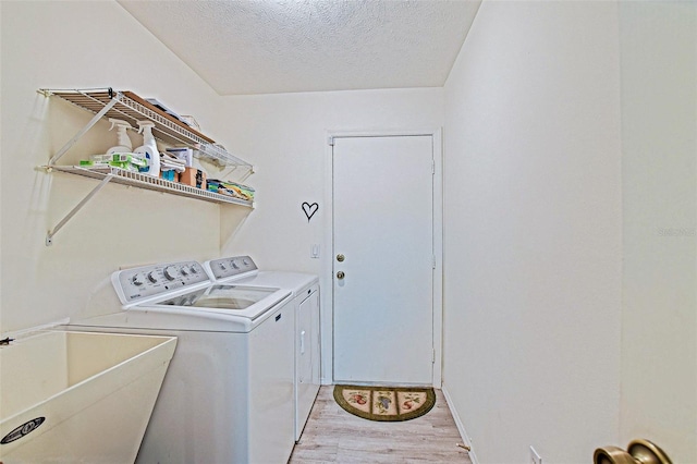 laundry area featuring washer and clothes dryer, light wood-type flooring, and a textured ceiling