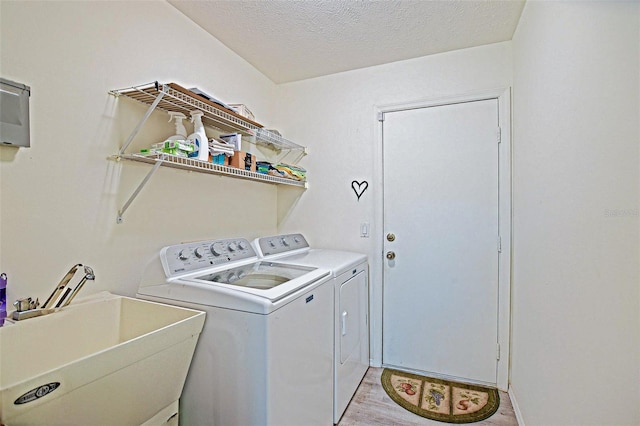 laundry room featuring washing machine and clothes dryer, a textured ceiling, and light wood finished floors