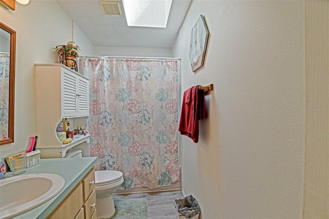 bathroom with vanity, a skylight, toilet, wood finished floors, and a shower with curtain