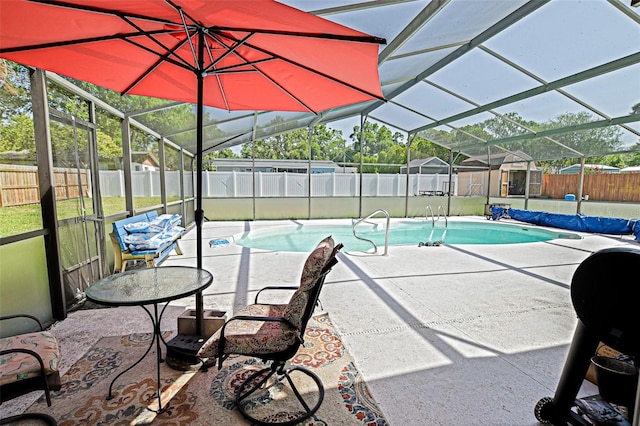 view of pool featuring a fenced backyard, glass enclosure, a patio, and a storage unit