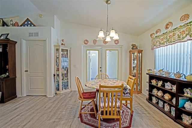 dining room with lofted ceiling, light wood finished floors, a chandelier, and french doors