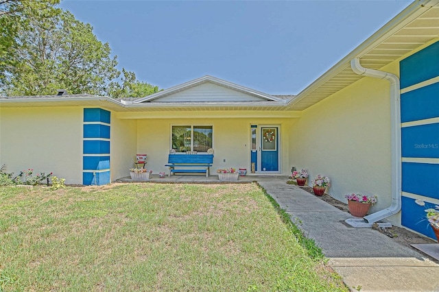 view of exterior entry with stucco siding and a lawn