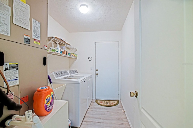 laundry room with a textured ceiling, heating unit, washer and clothes dryer, and light wood finished floors