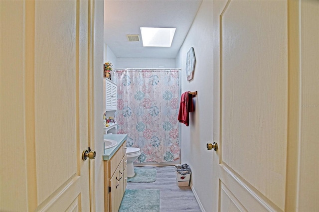 full bathroom featuring toilet, a skylight, vanity, wood finished floors, and a shower with shower curtain