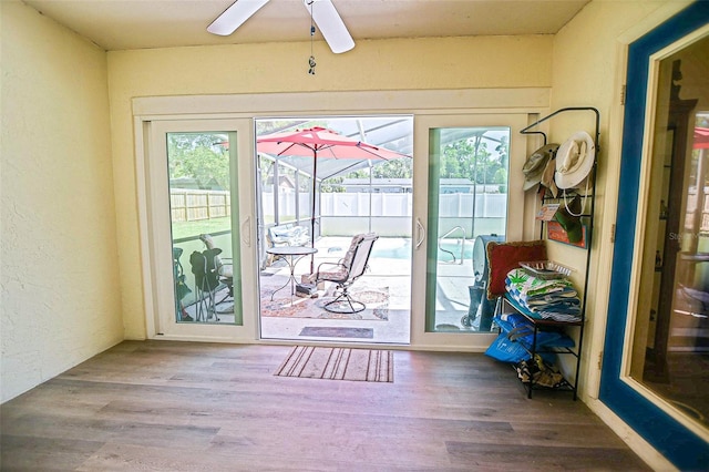 doorway to outside with ceiling fan, healthy amount of natural light, a sunroom, wood finished floors, and a textured wall