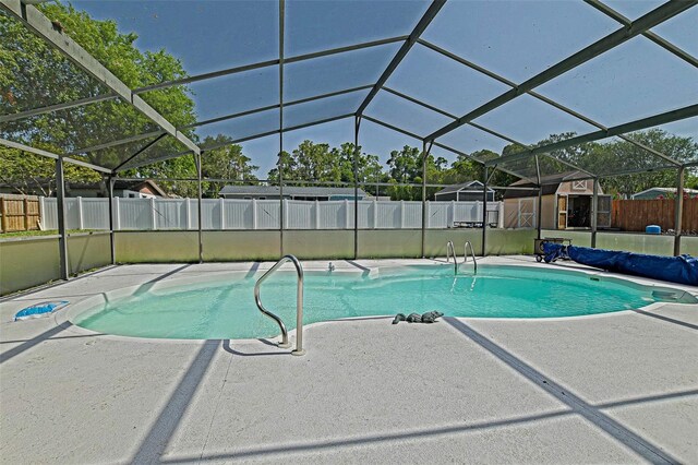 view of pool with a patio, a fenced backyard, a storage shed, and glass enclosure