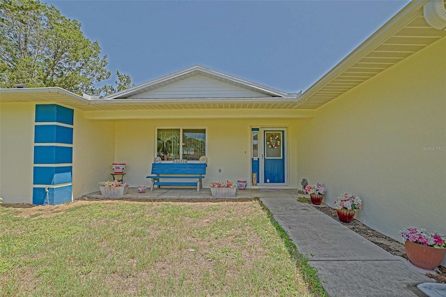property entrance with stucco siding, covered porch, and a lawn