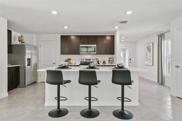 4955 SW 51st Rd, Gainesville, FL 32608 - kitchen with appliances with stainless steel finishes, light countertops, a breakfast bar area, dark brown cabinets, and a kitchen island with sink