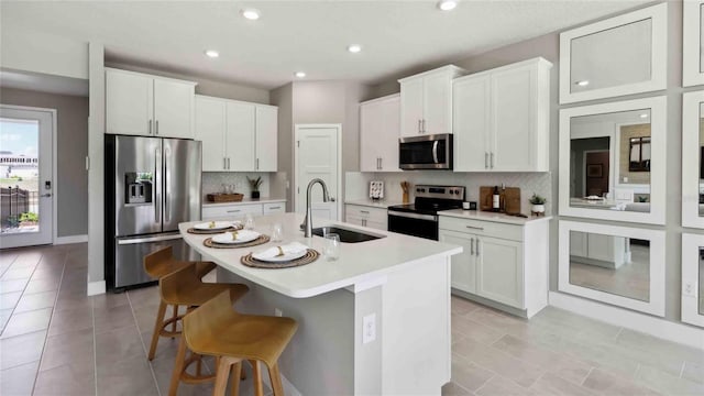 kitchen with stainless steel appliances, a sink, decorative backsplash, a kitchen breakfast bar, and a center island with sink