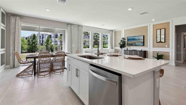 kitchen with dishwasher, a sink, light countertops, a center island with sink, and white cabinetry
