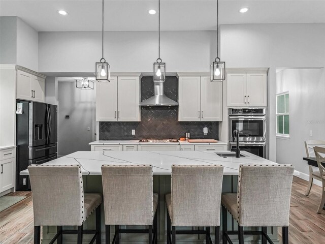 5330 NE 111th Lane Rd, Anthony, FL 32617 - kitchen featuring stainless steel appliances, wall chimney range hood, a kitchen island with sink, tasteful backsplash, and light wood finished floors