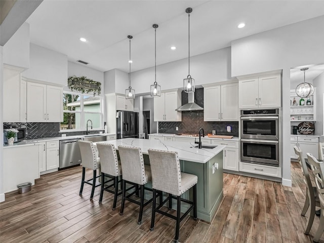 5330 NE 111th Lane Rd, Anthony, FL 32617 - kitchen featuring appliances with stainless steel finishes, wall chimney range hood, a kitchen island with sink, decorative backsplash, and white cabinets