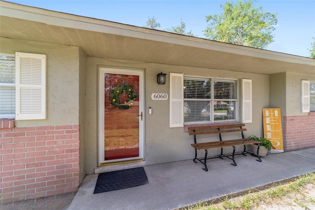 6060 SE 119th Pl, Belleview, FL 34420 - doorway to property featuring stucco siding, brick siding, and a porch