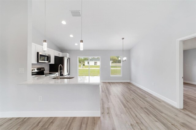 13779 SW 100th Ln, Dunnellon, FL 34432 - kitchen with appliances with stainless steel finishes, lofted ceiling, light wood-style flooring, white cabinetry, and hanging light fixtures