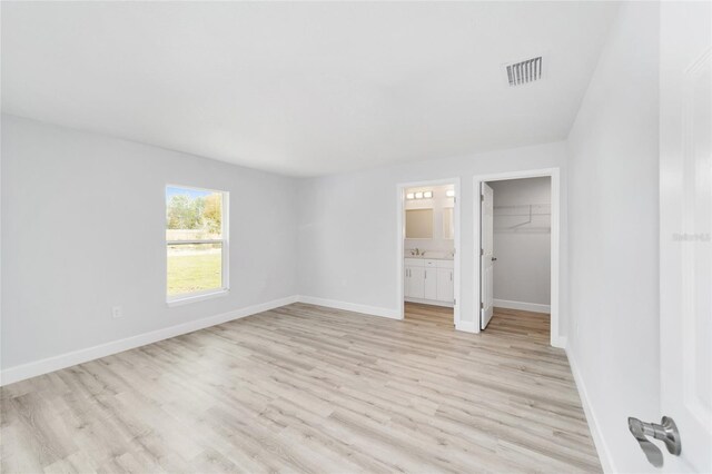13779 SW 100th Ln, Dunnellon, FL 34432 - unfurnished bedroom with light wood finished floors, a walk in closet, baseboards, a closet, and ensuite bath