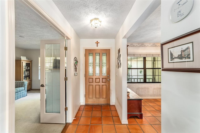 tiled entryway with a textured ceiling, baseboards, and carpet