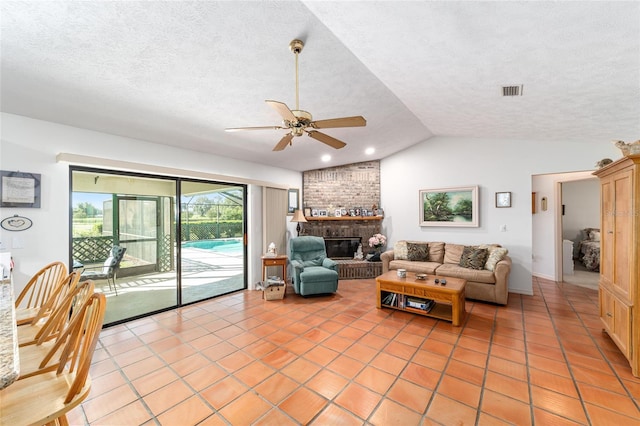 living room featuring ceiling fan, vaulted ceiling, a brick fireplace, a textured ceiling, and light tile patterned floors