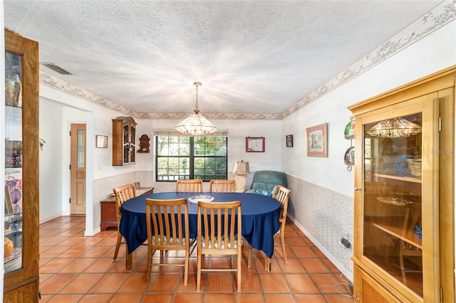 dining room with wallpapered walls, a chandelier, wainscoting, tile patterned flooring, and a textured ceiling