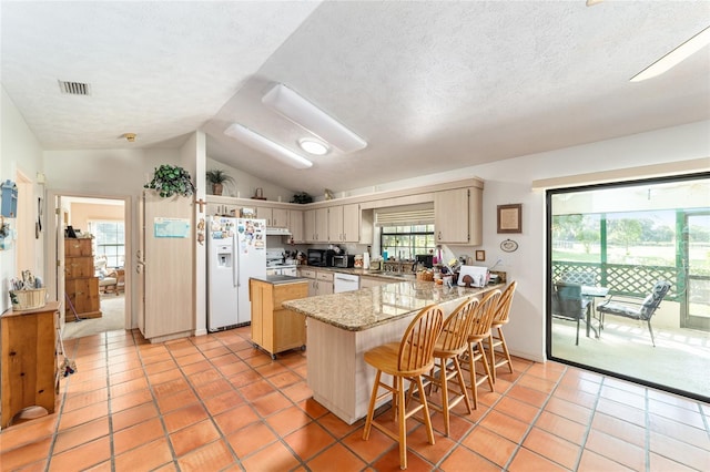 kitchen with white appliances, lofted ceiling, a peninsula, light tile patterned floors, and a center island