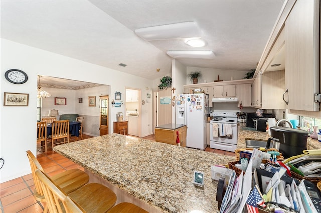 kitchen with white appliances, under cabinet range hood, light tile patterned floors, vaulted ceiling, and a peninsula