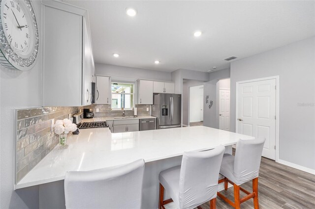 10427 SW 98th Place Rd, Ocala, FL 34481 - kitchen with appliances with stainless steel finishes, a peninsula, wood finished floors, decorative backsplash, and light countertops